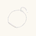 Delicate rhodium-plated silver chain bracelet with row of small baroque pearls centered on white background.