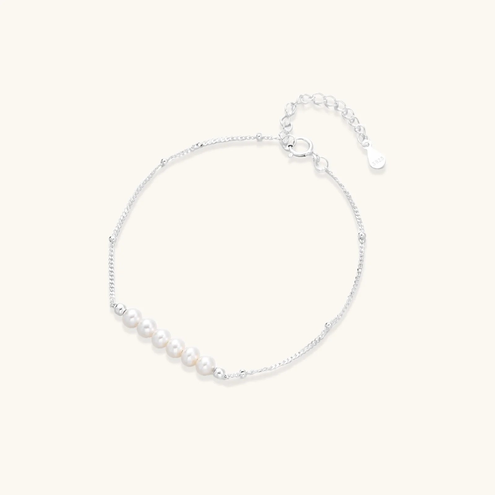 Delicate rhodium-plated silver chain bracelet with row of small baroque pearls centered on white background.
