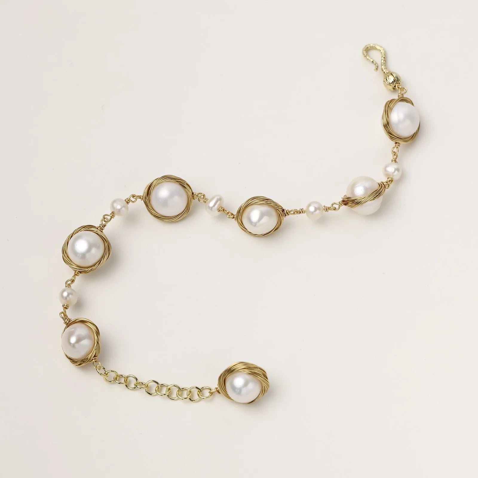 Gold wire-wrapped freshwater pearl bracelet with alternating pearl sizes on cream background, adjustable length