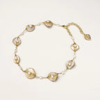 Gold-plated necklace with wire-wrapped shell pieces and freshwater pearls on neutral background, adjustable chain visible.