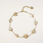 Gold-plated necklace with wire-wrapped shell pieces and freshwater pearls on neutral background, adjustable chain visible.