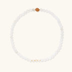 Three layered white beaded bracelets with carved orange agate lotus centerpiece and freshwater pearls on cream background.
