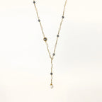 Y-shaped gold-plated necklace with white and gray freshwater pearls on cream background, showing adjustable drop design.