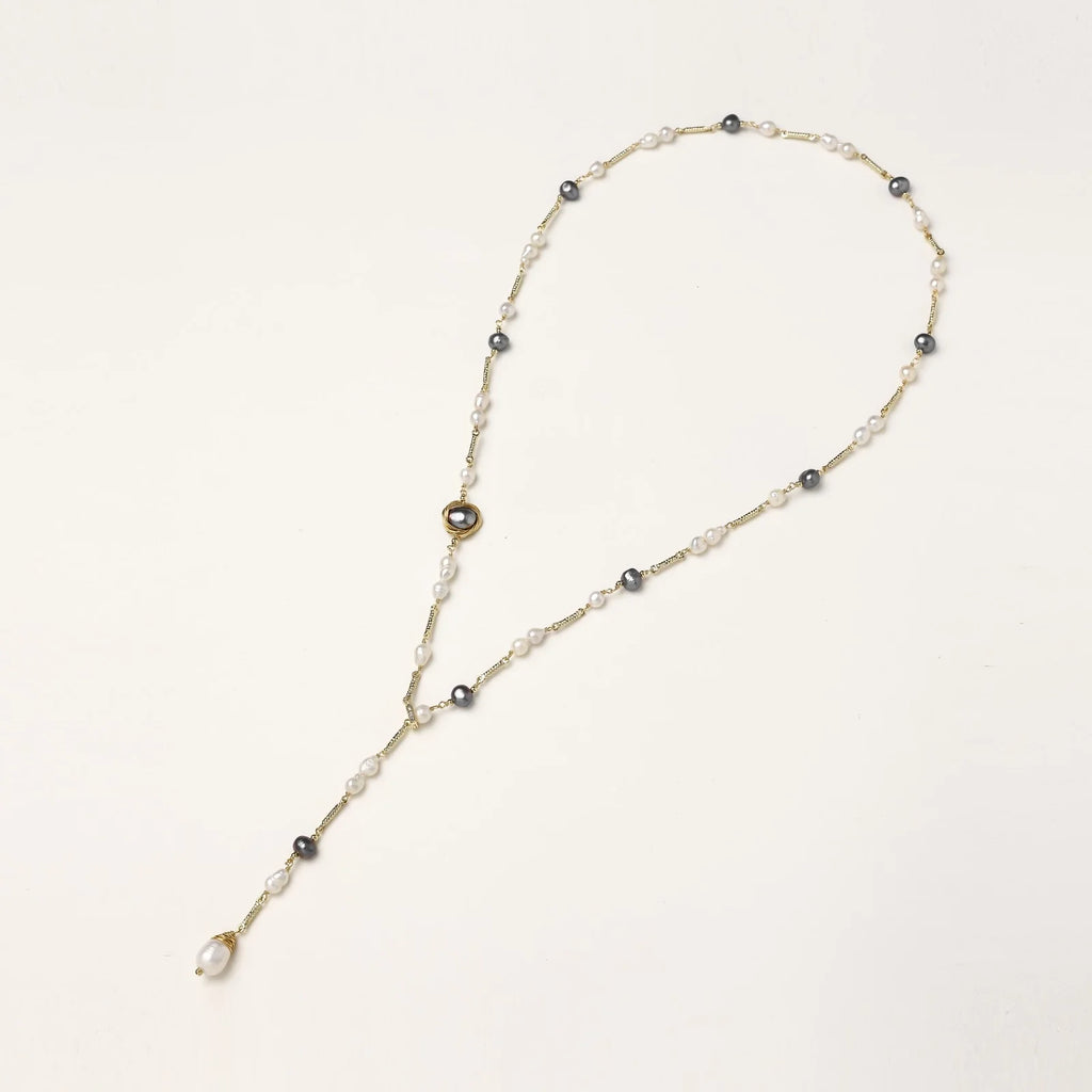Y-shaped gold-plated necklace with white and gray freshwater pearls on cream background, showing adjustable drop design.