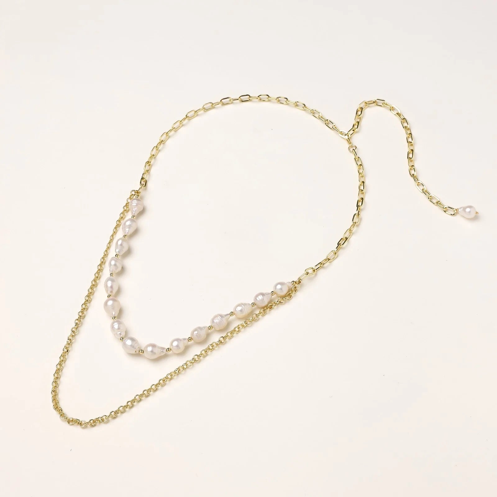 Layered gold chain necklace with organic baroque freshwater pearls and adjustable length on cream background