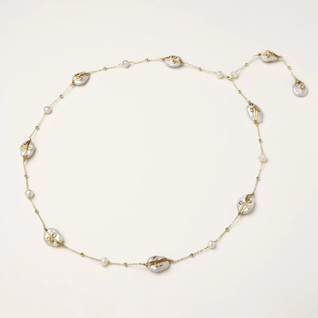 Long gold chain necklace with baroque pearls wrapped in leaf designs and small freshwater pearls spaced along the strand