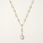 Y-shaped gold necklace with alternating geometric links, freshwater pearls, and baroque pearl pendant on cream background