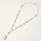 Y-shaped gold necklace with alternating geometric links, freshwater pearls, and baroque pearl pendant on cream background