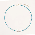 Delicate gold vermeil necklace with teal apatite beads and freshwater pearl on white background.