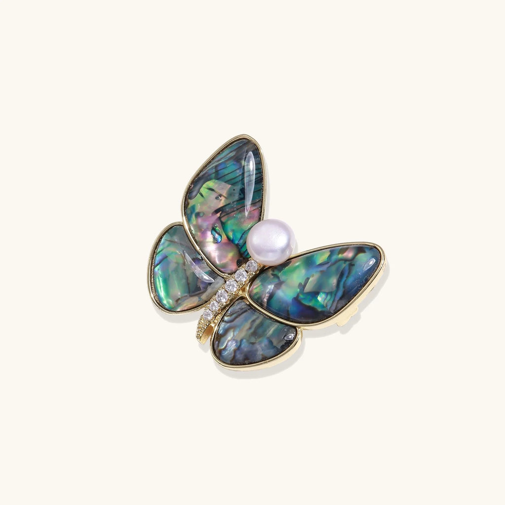 Gold-plated butterfly brooch with iridescent abalone shell wings and freshwater pearl accent on cream background.