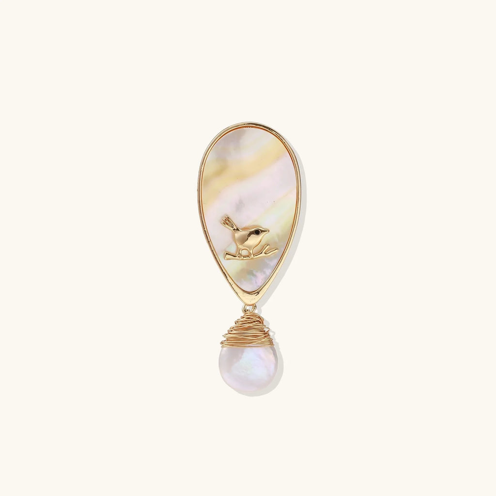 Iridescent shell brooch with gold bird accent and wire-wrapped baroque pearl drop on cream background.