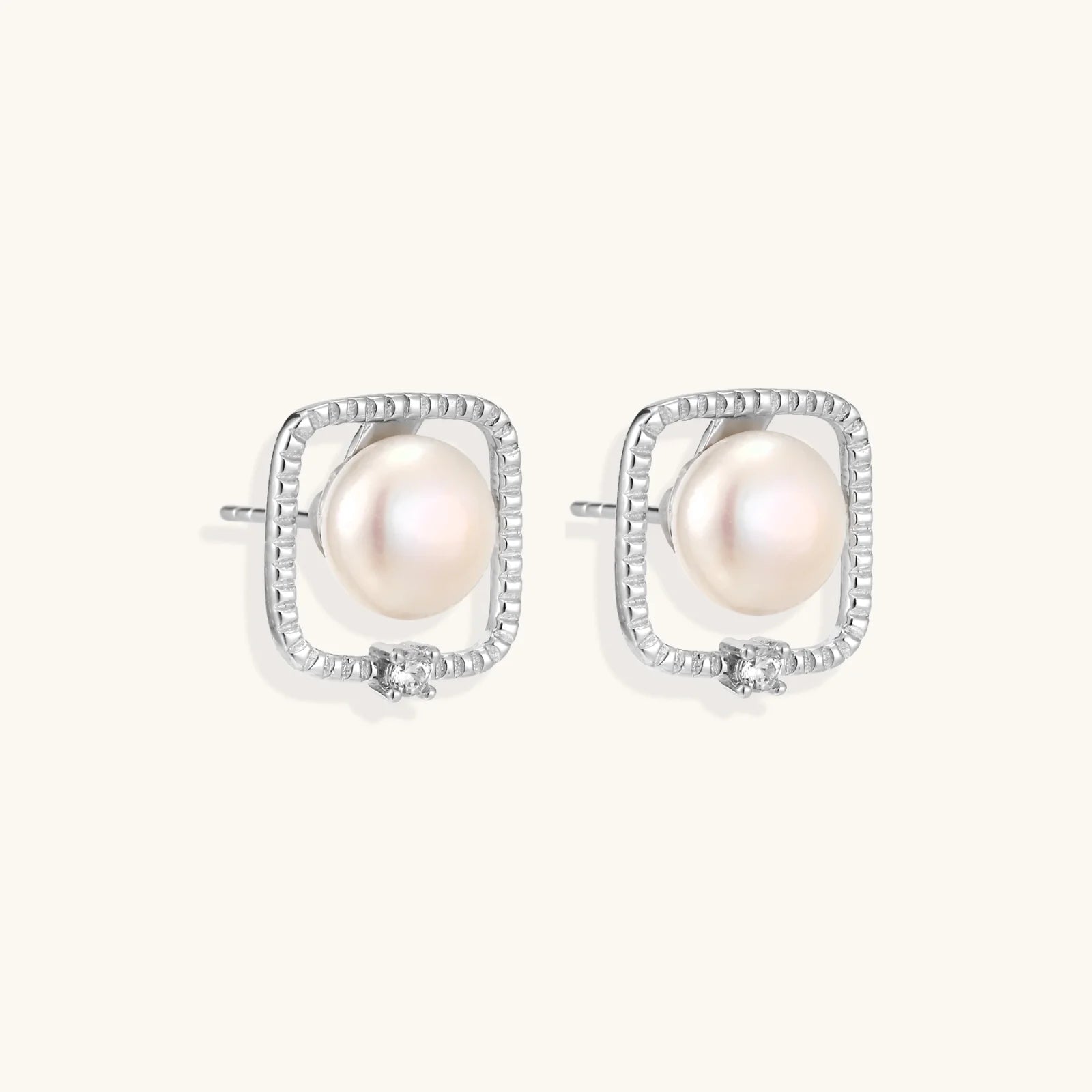 Rhodium-plated silver stud earrings with cushion frame, centered freshwater pearl, and tiny crystal accent