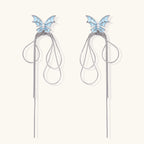 Long silver-tone earrings with powder blue enamel butterfly studs and flowing chain tassels on cream background