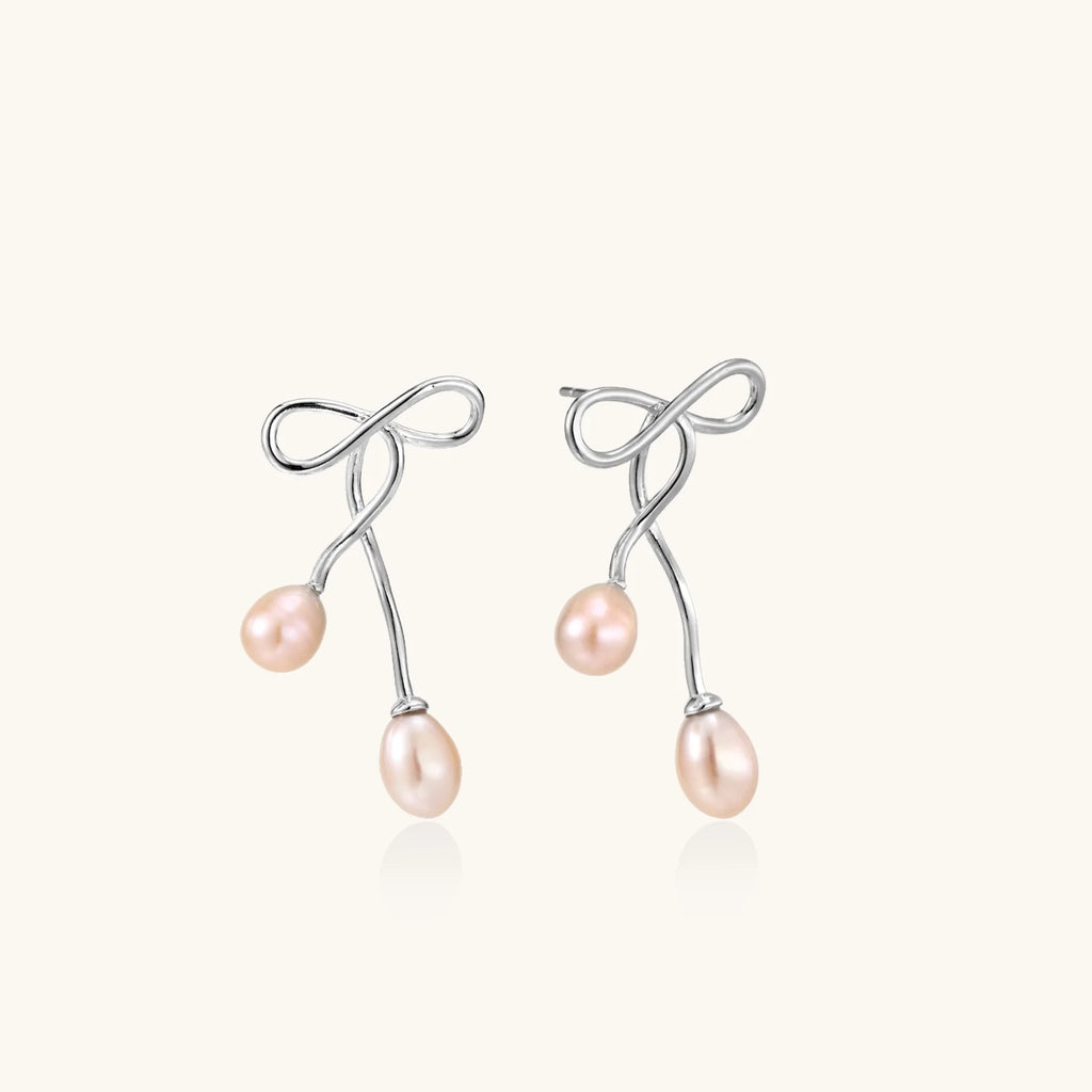 Rhodium-plated silver earrings with organic vine curves and two peachy freshwater pearls on cream background