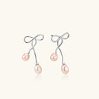 Rhodium-plated silver earrings with organic vine curves and two peachy freshwater pearls on cream background