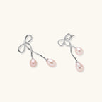 Rhodium-plated silver earrings with organic vine curves and two peachy freshwater pearls on cream background