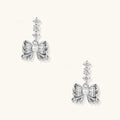 White gold plated drop earrings with three graduated zirconia crystals leading to a bow charm with pearl center