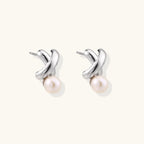 Rhodium-plated silver earrings with twisted X design and freshwater pearl drops on beige background