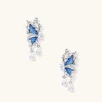 Silver butterfly earrings with blue denim fabric wings and dangling teardrop crystals on cream background