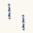 White gold-plated hoops intertwined with blue denim fabric in a twisted rope design on cream background.