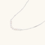 Delicate sterling silver chain necklace with small freshwater pearls arranged in a curved smile arc on cream background.