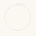 Delicate sterling silver chain necklace with small freshwater pearls arranged in a curved smile arc on cream background.