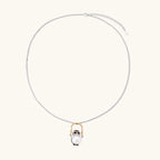 Whimsical owl pendant holding a white pearl on a gold swing, rhodium-plated silver chain on cream background.