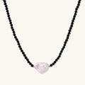 Beaded black agate necklace with iridescent baroque freshwater pearl centerpiece on cream background.