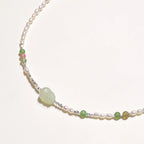 Delicate pearl necklace with pale green serpentine jade centerpiece and colorful agate beads on cream background