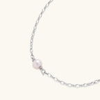 Dainty rhodium-plated silver chain necklace with centered 10mm freshwater pearl and crystal accents on cream background