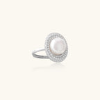 Silver ring with lustrous white pearl center surrounded by sparkling crystal halo on light background.