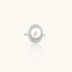 Silver ring with lustrous white pearl center surrounded by sparkling crystal halo on light background.
