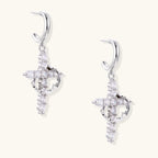 White gold-plated hoop earrings with sparkling zirconia cross charms dangling against cream background