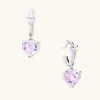 Silver huggie hoops with pink heart-cut zirconia pendants on white background, eco-friendly white gold plated brass