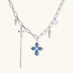 White gold plated chain necklace with blue textured cross pendant, spike charms, and mini cross detail on beige background