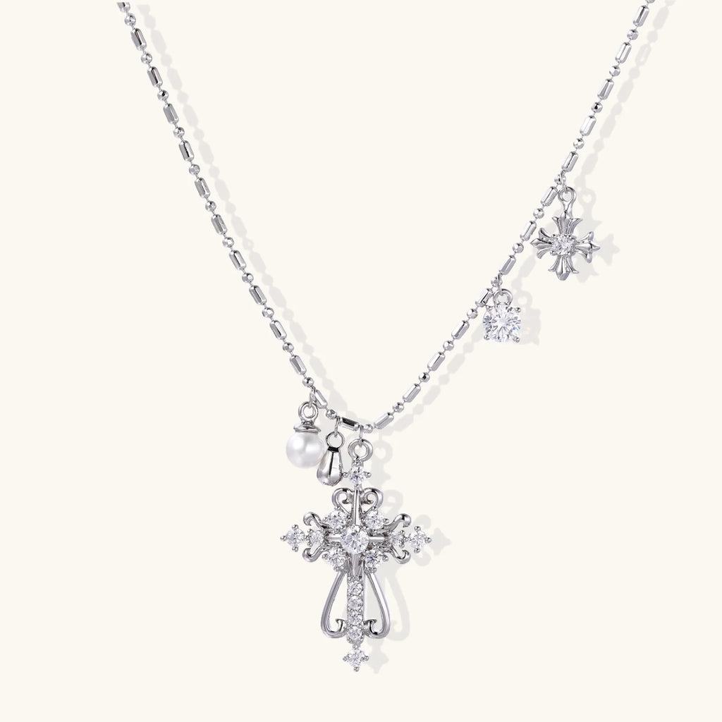 Ornate white gold-plated cross pendant with zirconia stones and pearl accents on adjustable silver chain against cream background