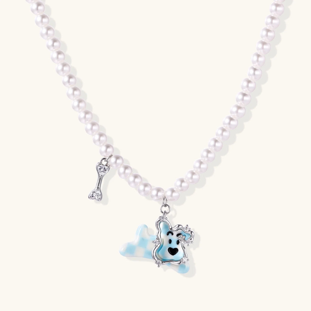 Pearl necklace with playful blue dog pendant accented with sparkly crystals on cream background.