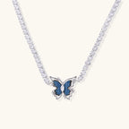 White gold plated tennis necklace with blue denim butterfly pendant and clear zirconia stones on cream background