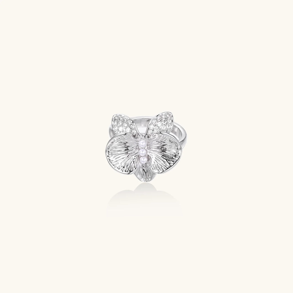 Silver-toned orchid ring with textured petals, pearl center accents, and sparkling zirconia stones on white background.