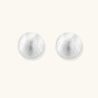 Brushed sterling silver half-dome clip-on earrings with textured surface against cream background