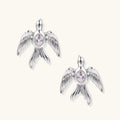 White gold-plated bird earrings with spread wings and oval zirconia center on cream background