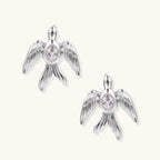 White gold-plated bird earrings with spread wings and oval zirconia center on cream background