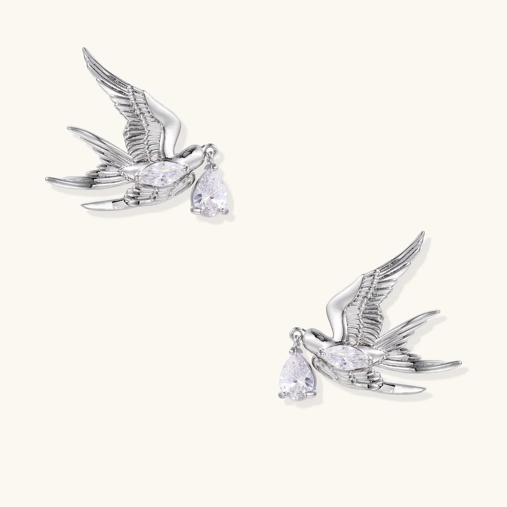 Silver-toned swallow stud earrings with detailed wings carrying teardrop zirconia crystals on white background