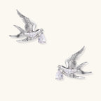 Silver-toned swallow stud earrings with detailed wings carrying teardrop zirconia crystals on white background