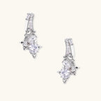 White gold-plated huggie earrings with geometric emerald-cut zirconia clusters in starburst formation on beige background