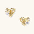 Pair of sculptural gold-plated wing stud earrings with zirconia stones on cream background, showing dimensional feather design