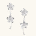 Silver-white asymmetric earrings with textured flower petals and crystal centers on cream background