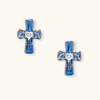 White gold-plated cross earrings with blue enamel, bat wing details, and heart-shaped zirconia center on cream background.