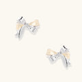 Dimensional bow stud earrings in white gold plated brass with silver and cream two-tone finish on neutral background