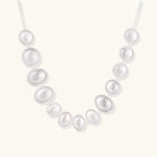 Graduated pearl-finish silver discs forming an organic bubble bib necklace on delicate chain against cream background.
